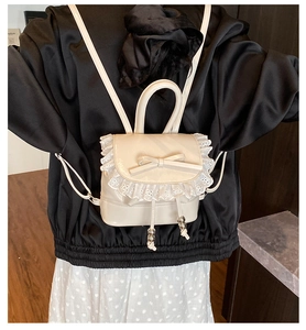 Detalle de una mini mochila crema con bordes de encaje y lazo de cuero en una modelo