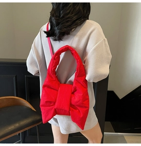 Detail of a red bow-shaped quilted shoulder bag with plush fabric and long strap