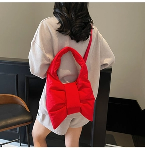 Detail of red bow-shaped quilted nylon shoulder bag on model for casual commuting look