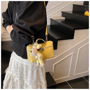 Detail of yellow lychee leather box bag featuring a cute plush dog charm on crossbody strap