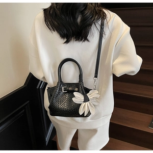 Détail du sac tressé noir avec breloque fleur blanche porté par un mannequin