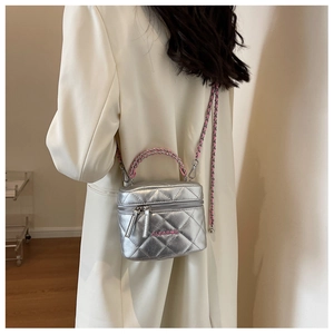 Detail of silver quilted box bag with chain strap and pink logo over a white blazer
