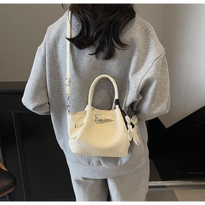 Détail d'un sac à main tressé crème avec breloque fleurie et bandoulière réglable