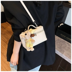Close-up of white lychee leather box bag with cute dog charm and detachable shoulder strap