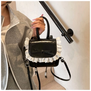 Detail of black patent leather mini bag with white lace trim and bow accentuation