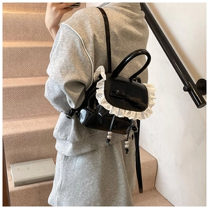 Detail of black patent leather backpack with white lace trim and bow on front flap