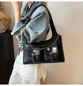 Detail of black matte leather shoulder bag featuring silver chains and heart charms