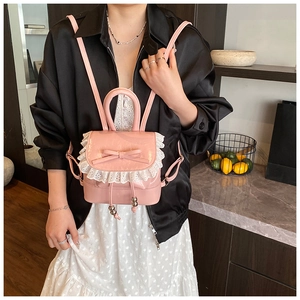 Detail of a pink mini faux leather backpack with lace trim and ribbon bow on model