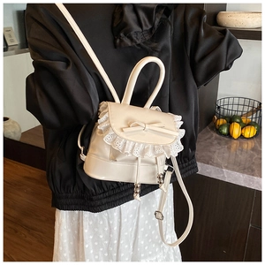 Primer plano de una pequeña mochila crema con volantes de encaje y lazo en modelo