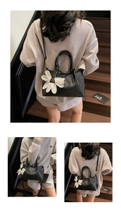Detail of black woven handbag featuring a white floral charm and adjustable shoulder strap