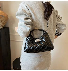 Détail d'un sac en cuir verni matelassé avec boucle argentée tenu par un mannequin chic