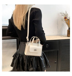 Detailed view of cream-colored minimalist handbag with silver buckle in a modern setting
