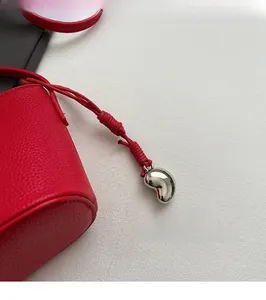 Detail of red pebbled leather bag featuring a silver bean pendant and braided lanyard