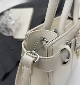 Gros plan sur la boucle argentée et les coutures d'un sac à main en cuir crème