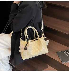 Detail of cream woven bucket bag featuring large silk flower charm and slim strap