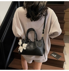 Detail of black woven bucket bag with white bow charm on a model in lifestyle setting