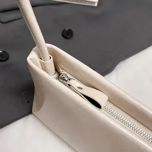 Close-up of premium silver hardware zipper and leather puller on cream shoulder bag