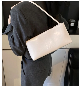 Detail view of a glossy white baguette shoulder bag with embossed fashion lettering
