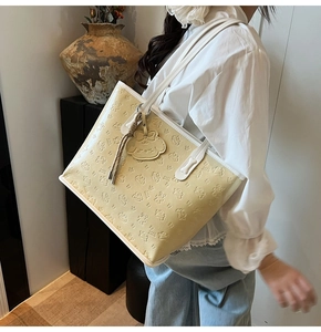 Détail d'un sac cabas beige avec motifs de dessins animés embossés et breloque assortie