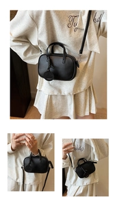 Detail of black pebbled leather mini pillow bag with dual handles and round smile charm