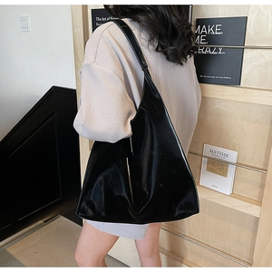 Close-up of a large black patent leather hobo bag worn by a model in a minimalist setting