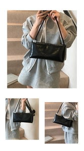 Detail of glossy black baguette bag featuring transparent bead strap decor and embossed logo