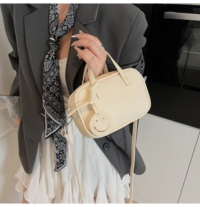 Close-up of mini crossbody bag in cream leather featuring a smiley charm and long strap