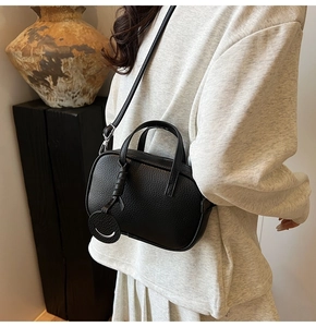 Detail of black pebbled leather crossbody bag with smiling pendant on model