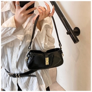 Détail d'un sac sous le bras en cuir verni noir brillant avec un fermoir rotatif doré