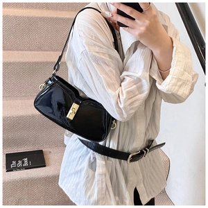 Détail d'un sac sous le bras en cuir verni noir avec un fermoir doré carré rotatif