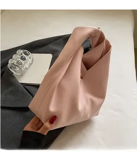 Detail of pink faux leather handbag with knot handle resting on white sheets and blazer