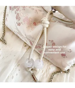 Close-up of beige floral bolster bag with silver zipper and beaded leather pull detail