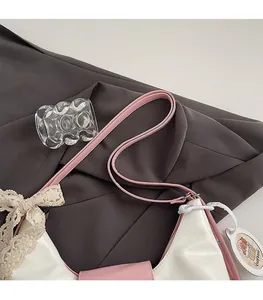 Détail d'un sac à bandoulière blanc brillant avec bord rose, nœud et badge Capybara