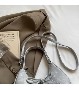 Sac bandoulière argenté en forme de croissant avec nœud et sangle réglable sur un drap
