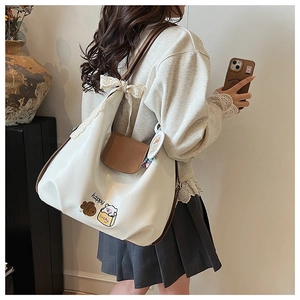 Détail du sac cabas blanc avec illustration d'ours, rabat marron et nœud en dentelle