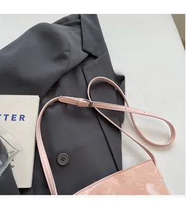Gros plan du sac seau en cuir verni rose avec motif floral gaufré et longue bandoulière