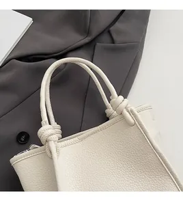 Close-up of cream white leather bucket bag with knotted handle and litchi texture