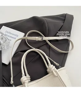 Detail of off-white lychee leather handbag with woven rope handle on grey blazer