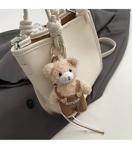 Macro detail of brown plush bear charm with corduroy overalls on white leather handbag