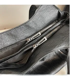 Close-up of dual silver zippers and textured black leather surface of the tote bag