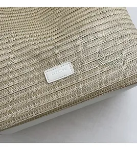 Detailed close-up of woven straw texture and white leather logo patch on tote bag