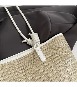 Close-up of woven straw tote bag with white faux leather trim and knotted handle details