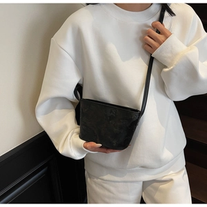 Détail d'un sac à bandoulière en cuir noir embossé porté par un mannequin en tenue décontractée