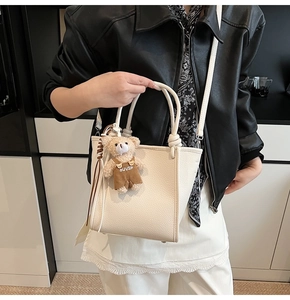 Detail view of cream bucket bag in pebble leather with brown plush bear charm