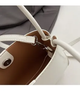 Detailed close-up of white leather bucket bag with silver magnetic clasp and brown lining