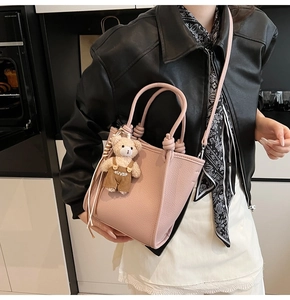 Detail of pink lychee leather handbag with a cute bear charm and thin shoulder strap