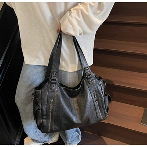 Close-up of black matte tote bag with lychee texture and silver zipper details on wood stairs