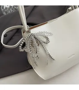 Detail of white leather bucket bag with CLEAR OK logo and beaded bow charm accessory