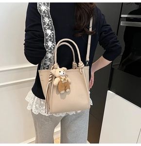 Chic beige lychee textured handbag with a cute teddy bear charm on a female model