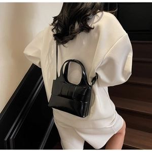 Détail d'un sac à main noir brillant structuré avec une anse et une fine bandoulière
